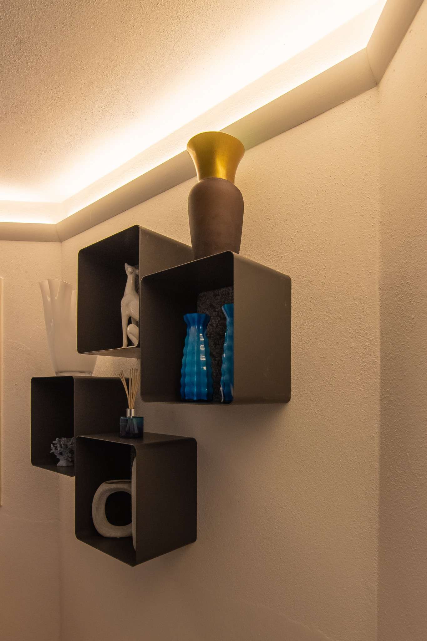 Illuminazione indiretta con Veletta® VE201 applicata all’angolo del soffitto, sopra mensole moderne con vasi decorativi.